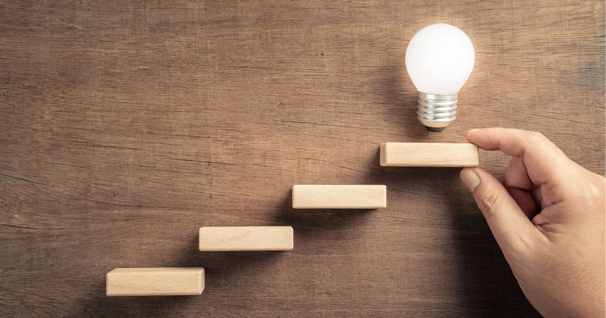 image of 4 steps against a wall with a lightbulb on the top step and a hand holding onto the step with two fingers to show How to Fix an Underperforming Sales Team in 4 Steps